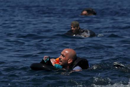 Un profugo siriano porta suo figlio in braccio mentre nuota al largo dell’isola di Lesbo, in Grecia, dopo che il gommone su cui viaggiavano è naufragato